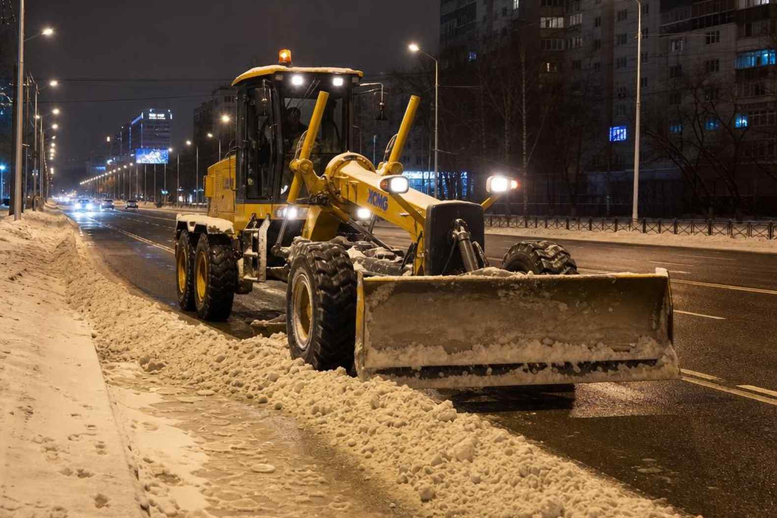 Автогрейдер за зимней снегоуборкой городской дороги - ночная смена